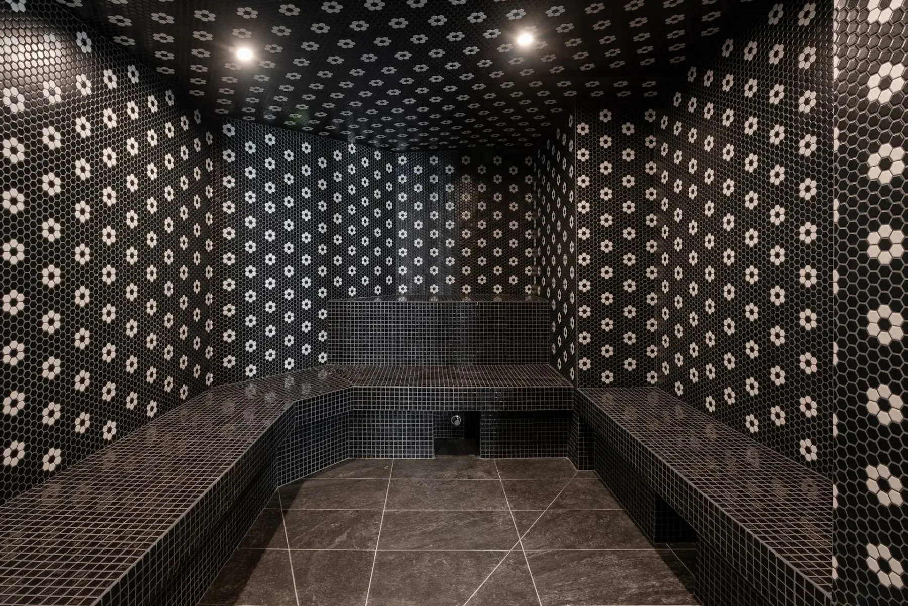 Modern indoor shower area with dark gray tiles, multiple shower heads, and recessed lighting.