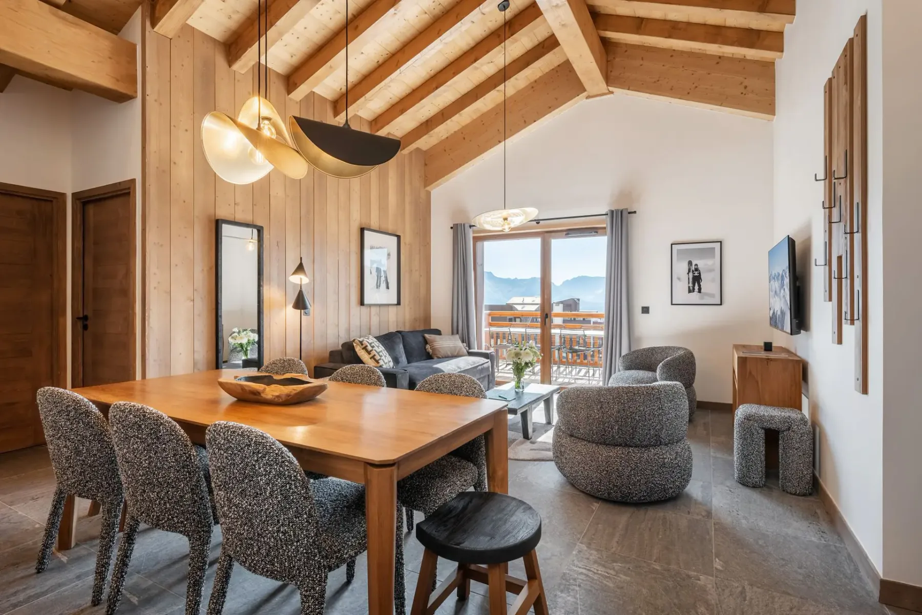 A cozy living room with wooden beams, modern furniture, a dining table, and large windows offering a mountain view.