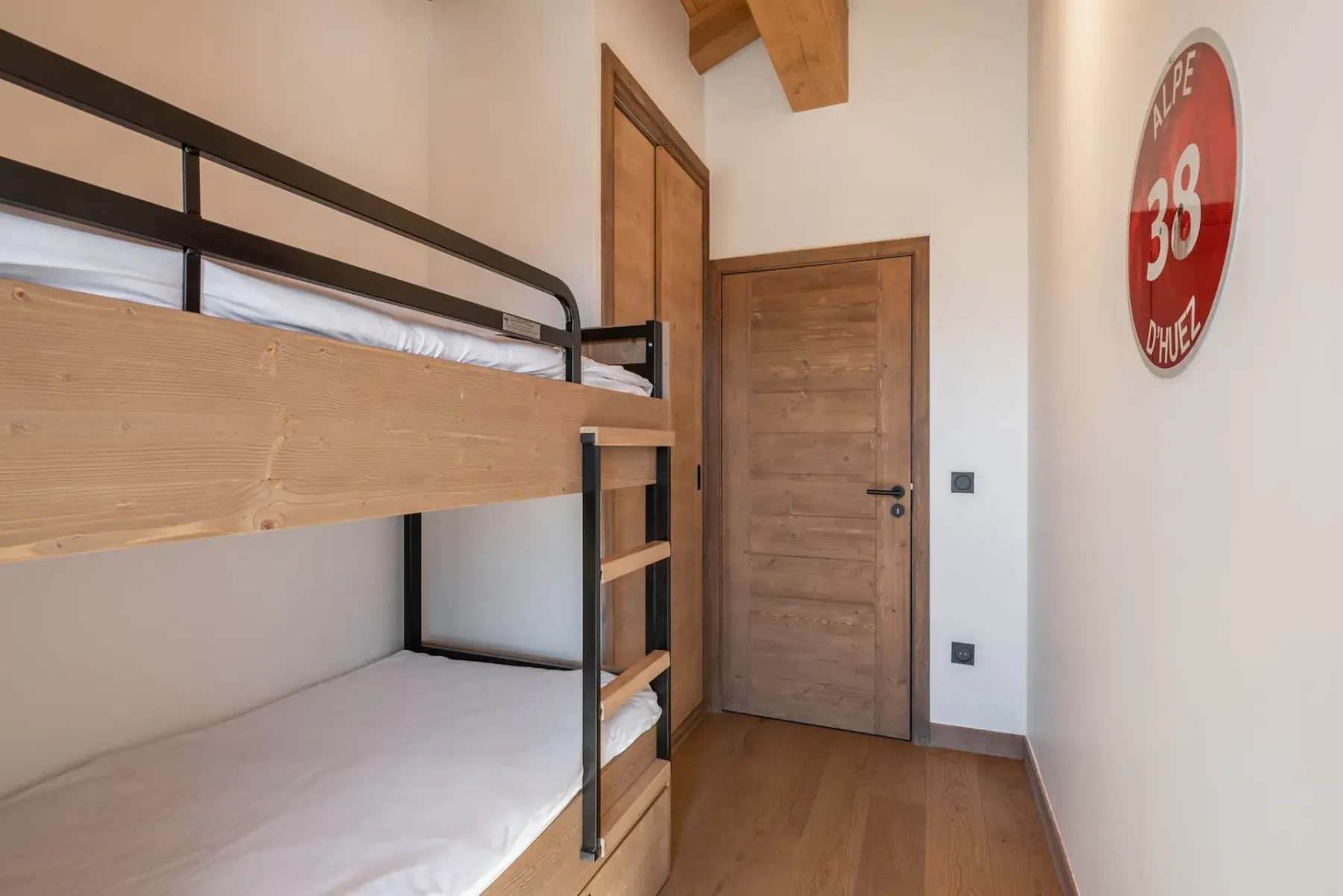Narrow room with wooden bunk beds, wooden ceiling, and a door leading to a balcony with mountain views. Daylight fills the space.
