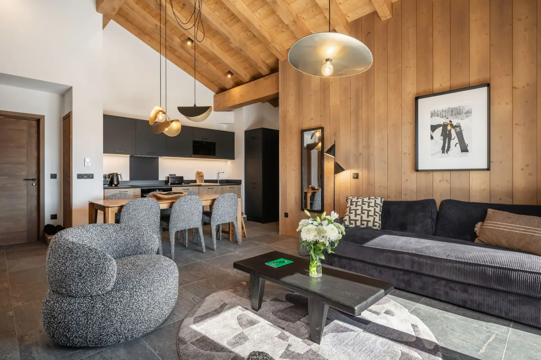 A cozy living room with wooden beams, modern furniture, a dining table, and large windows offering a mountain view.