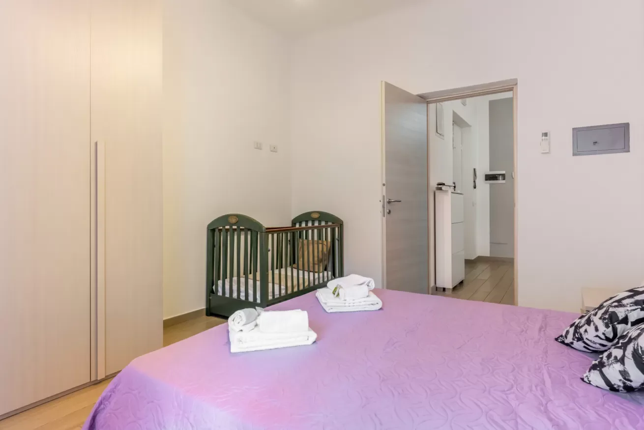 Un dormitorio con una colcha rosa y una cuna pequeña junto a la cama.