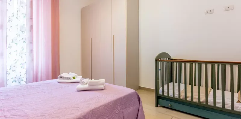 Un dormitorio con una cama cubierta de rosa, un armario y una cuna.