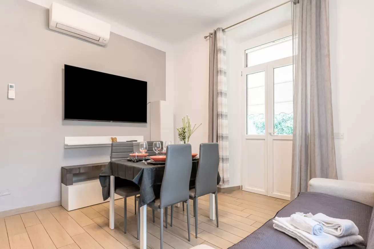 Comedor con una mesa y sillas junto a un televisor y puertas de vidrio.