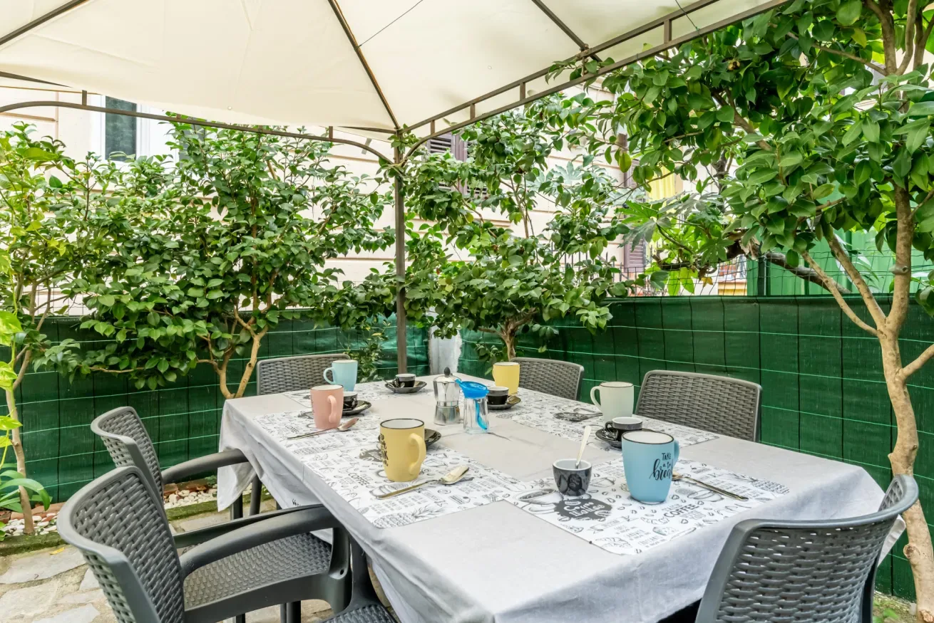 Comedor de jardín con una mesa larga bajo un toldo, rodeada de plantas frondosas.