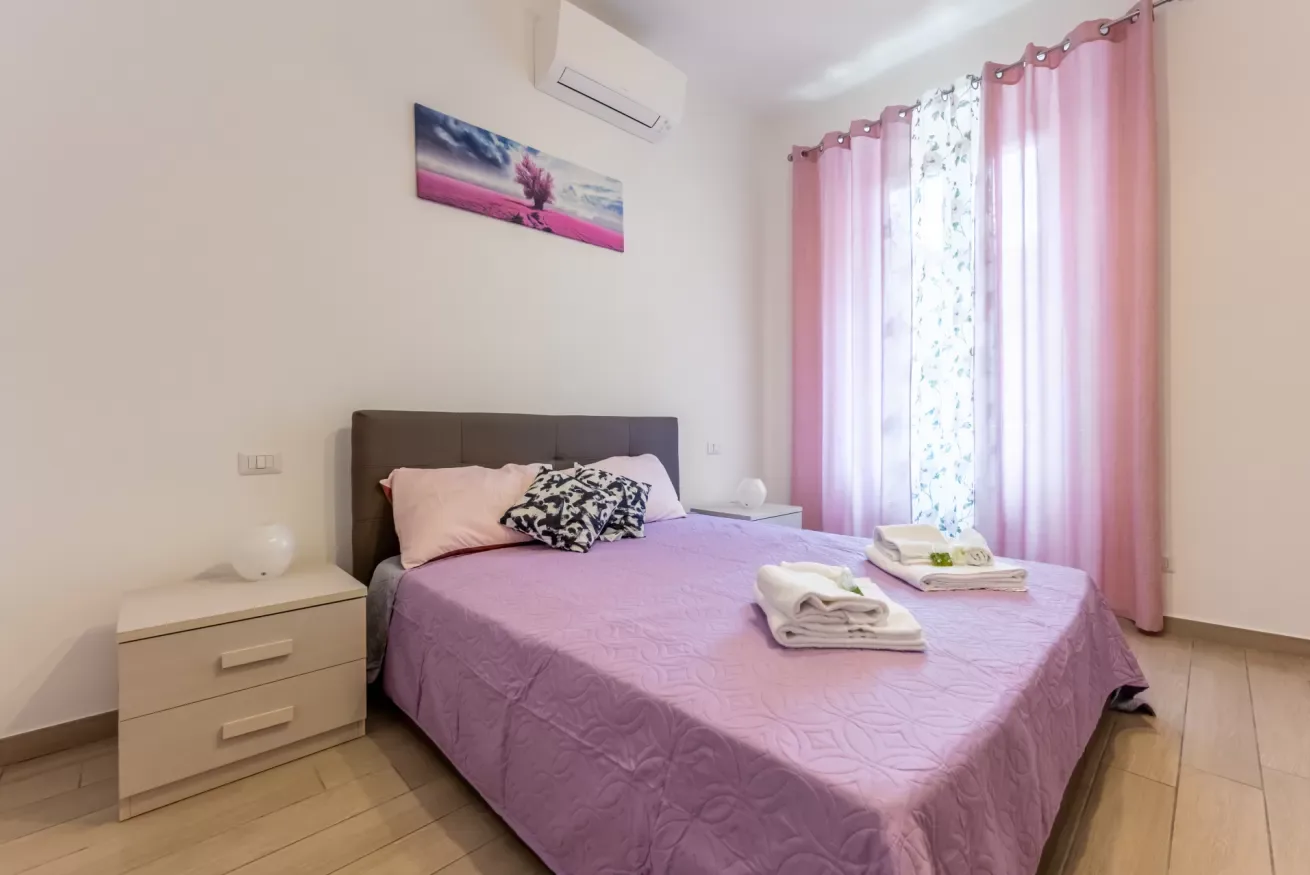 Un dormitorio con una cama vestida de rosa y cortinas junto a la ventana.