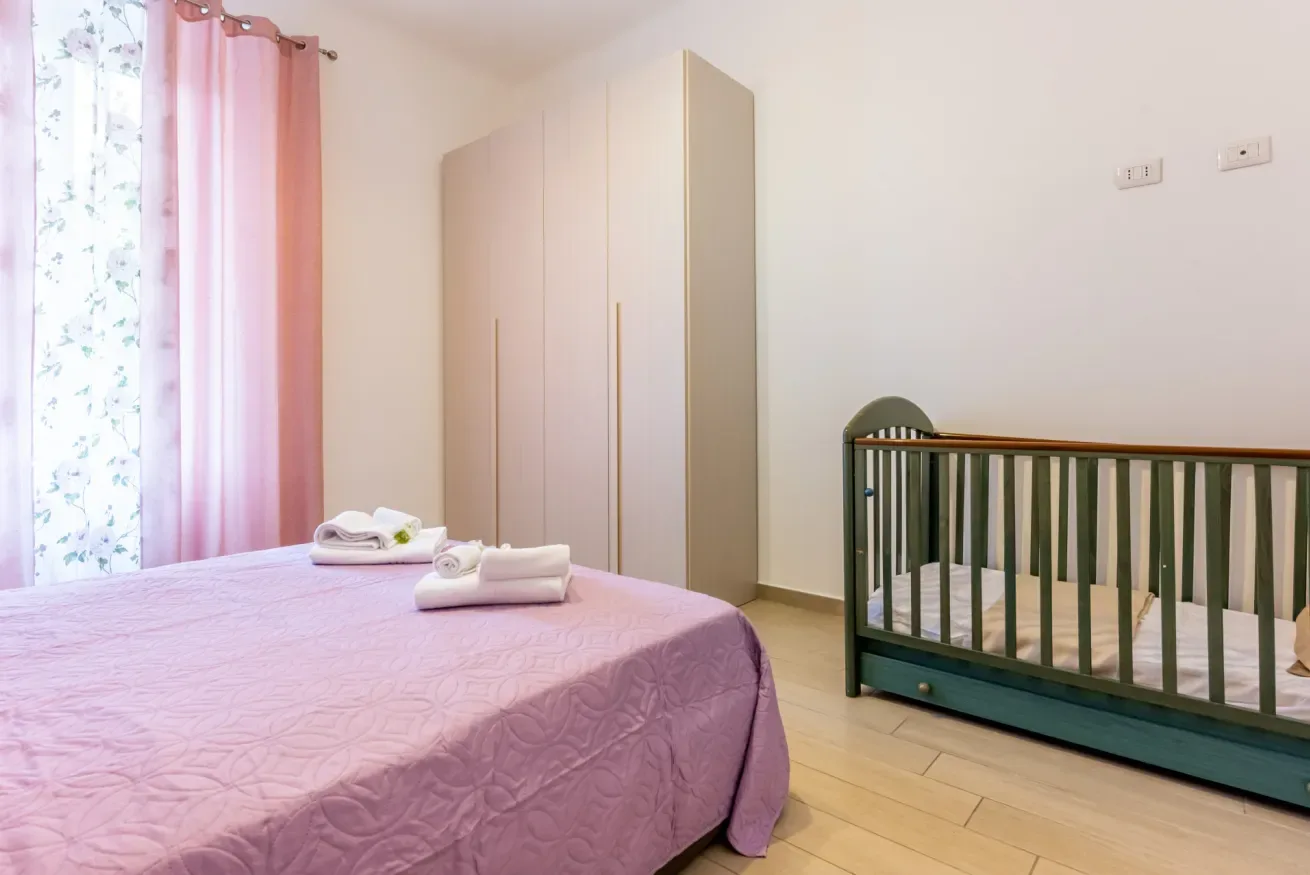 Un dormitorio con una cama cubierta de rosa, un armario y una cuna.