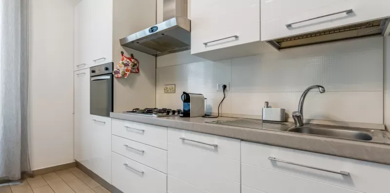 Una cocina luminosa con gabinetes blancos y una encimera junto a la pared.