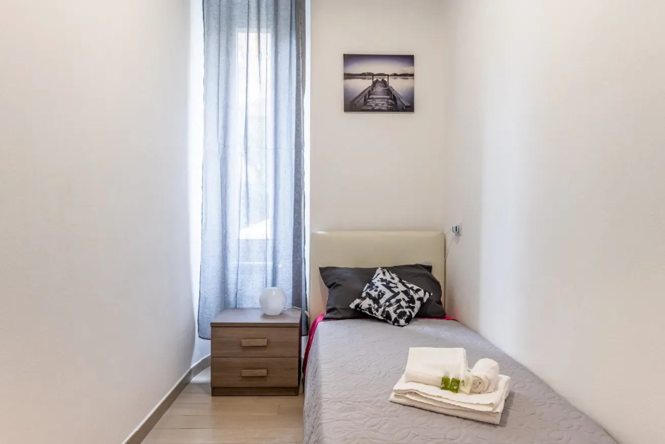 Una cama individual está junto a una ventana con cortinas en un dormitorio pequeño.