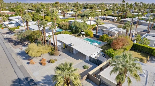 Vista aérea de un barrio residencial con edificios bajos, palmeras y una piscina.
