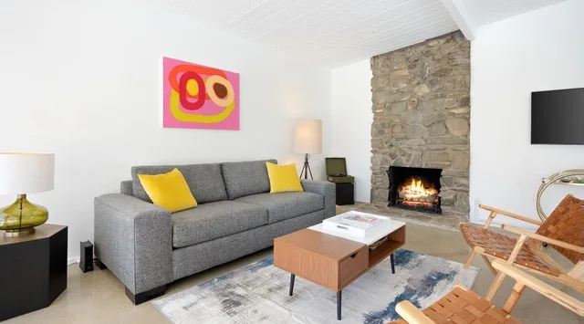 Una sala luminosa con asientos grises, una chimenea de piedra y arte colorido en la pared.