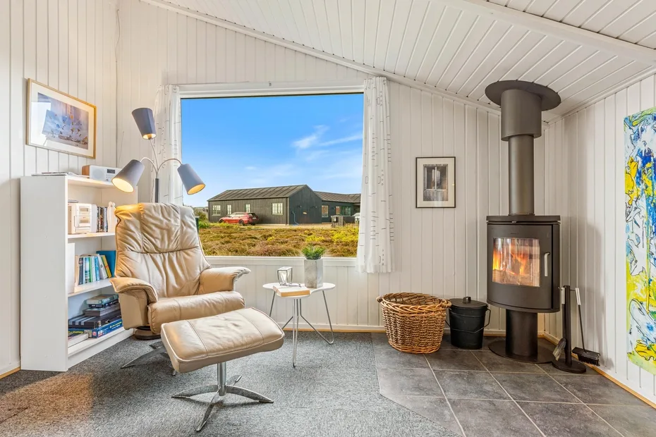 Una sala luminosa con un sillón reclinable junto a una ventana y una estufa de leña.