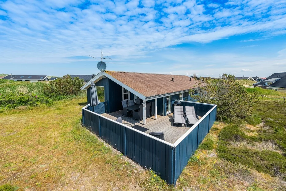 Una casa tiene una terraza elevada con asientos al aire libre y vistas a zonas verdes.