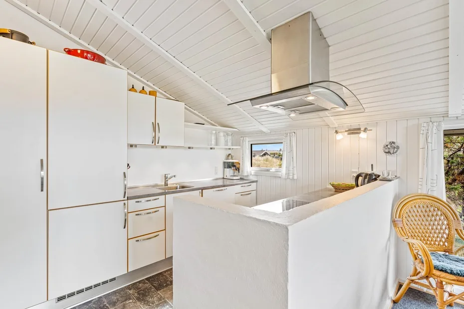 Una cocina blanca y luminosa con una isla central y una campana extractora de acero inoxidable.