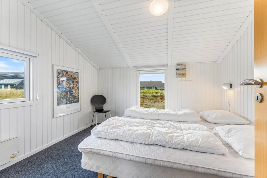 Un dormitorio luminoso con ropa de cama blanca y ventanas que dan a una zona de césped.