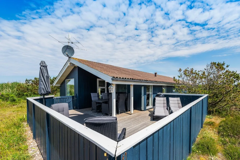 Una casa da a una terraza de madera con asientos al aire libre y una barandilla azul.