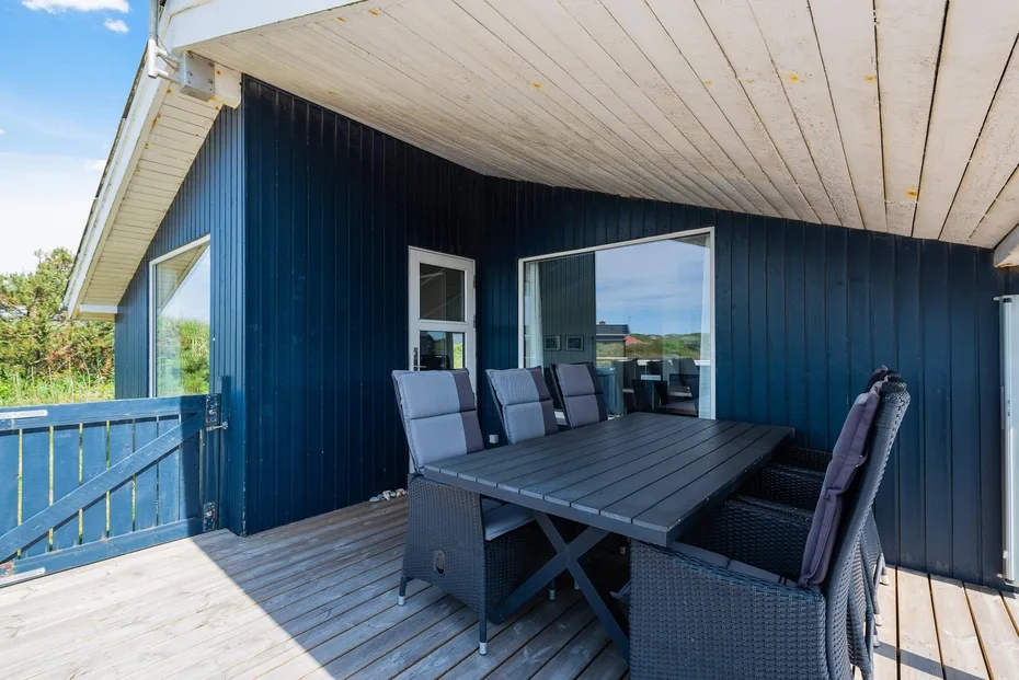 Comedor exterior cubierto con mesa y asientos junto a una casa azul.