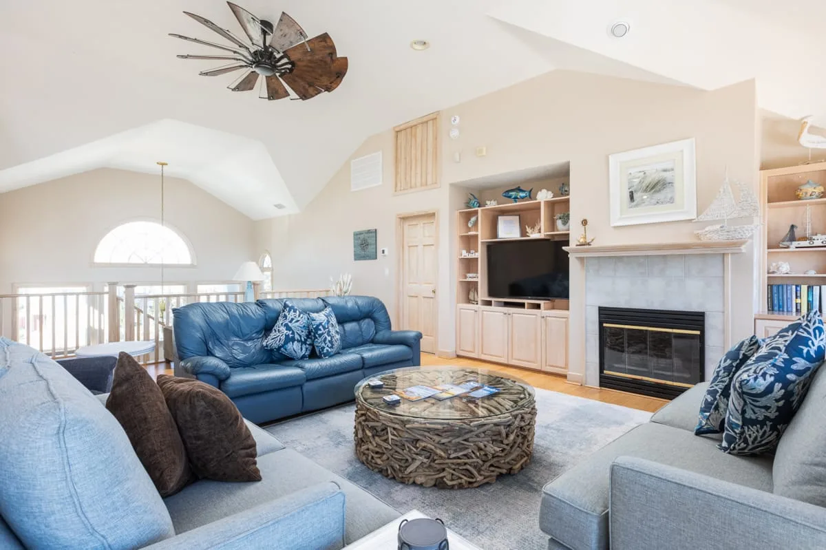 A bright living room with blue seating, a round coffee table, and a fireplace.
