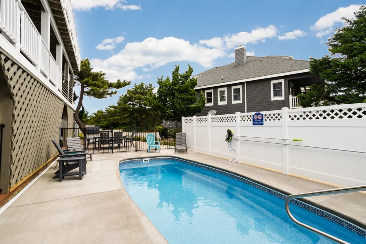 An outdoor swimming pool sits beside a paved deck and white fence.