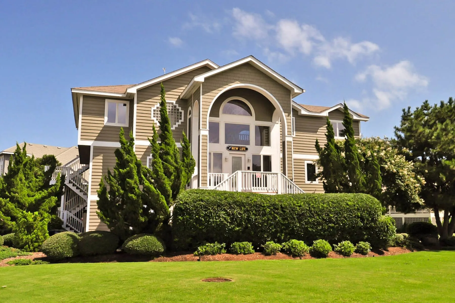 A large residential building with a prominent arched entrance faces a landscaped lawn.