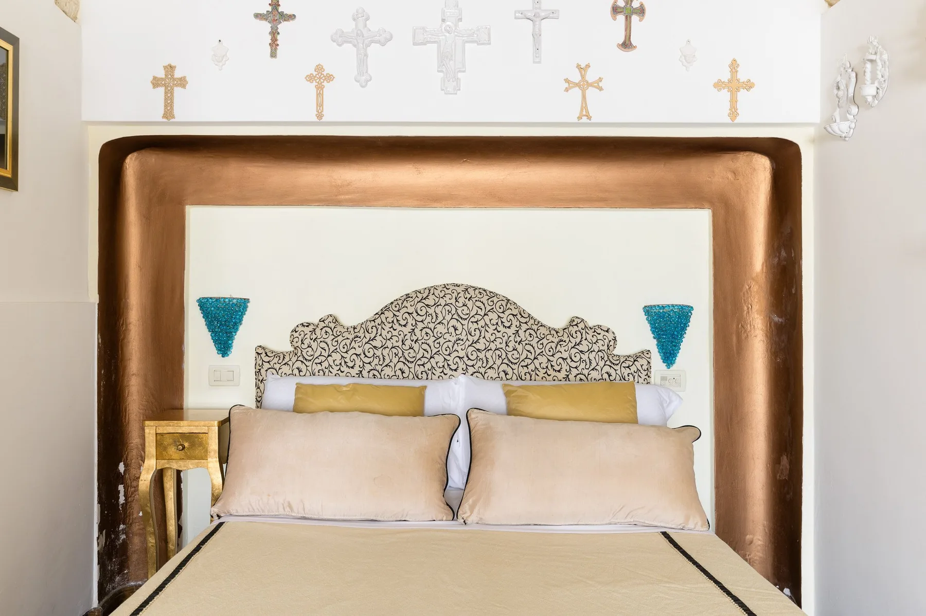 Un dormitorio con una cama, un cabecero ornamentado y cruces decorativas en la pared.