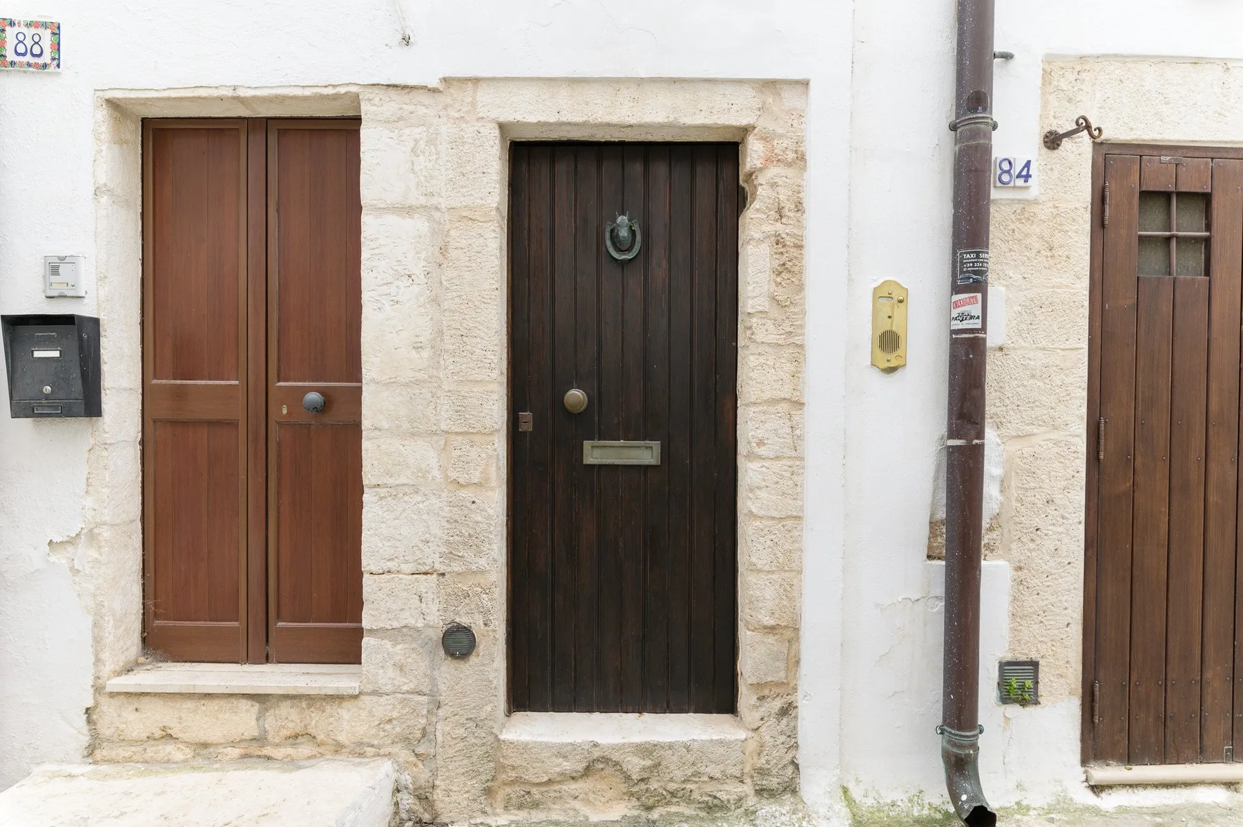 Entrada de edificio a la calle con puertas de madera oscura en piedra clara.