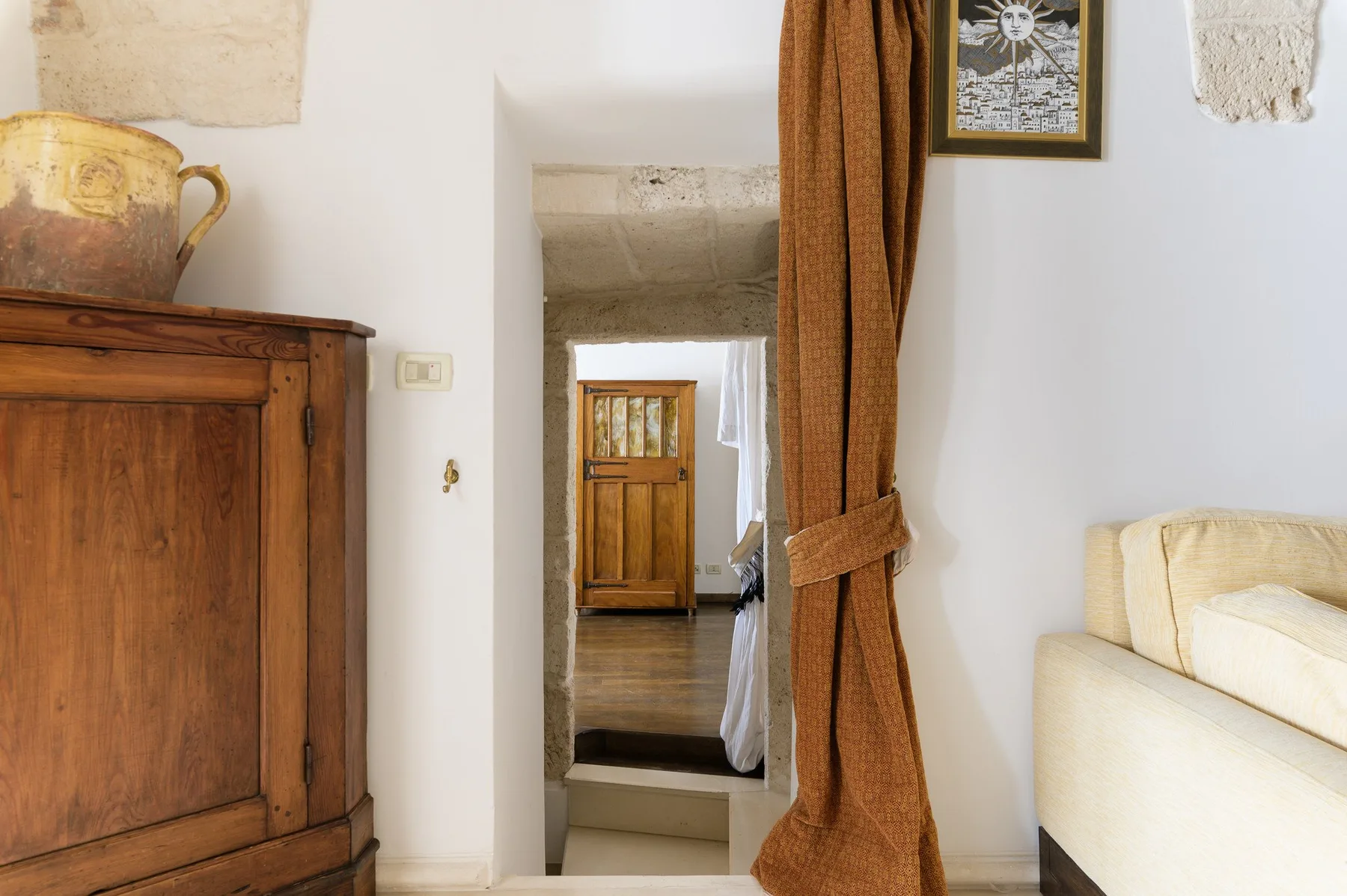 Una habitación luminosa con un mueble de madera, asientos crema y una puerta con cortina.