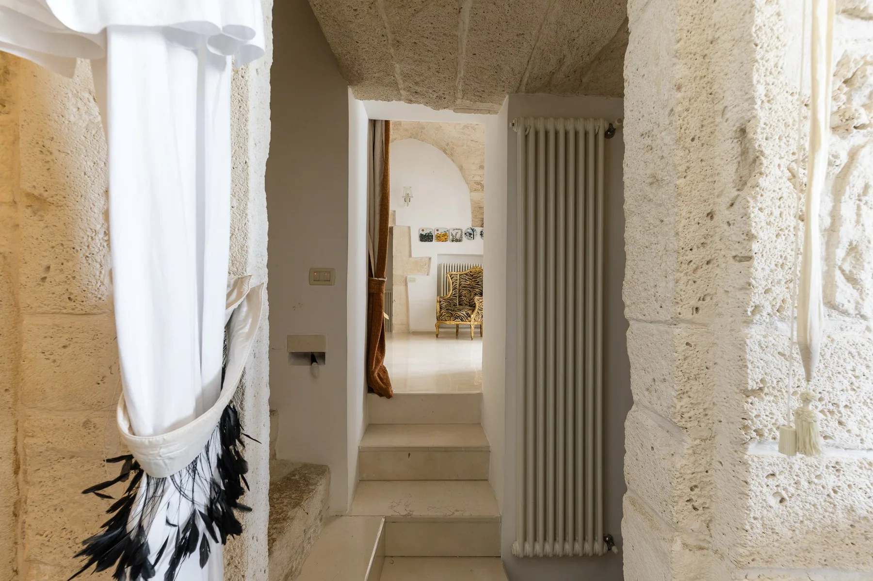 Un pasillo interior de piedra con una ventana con cortina y una puerta hacia otra habitación.