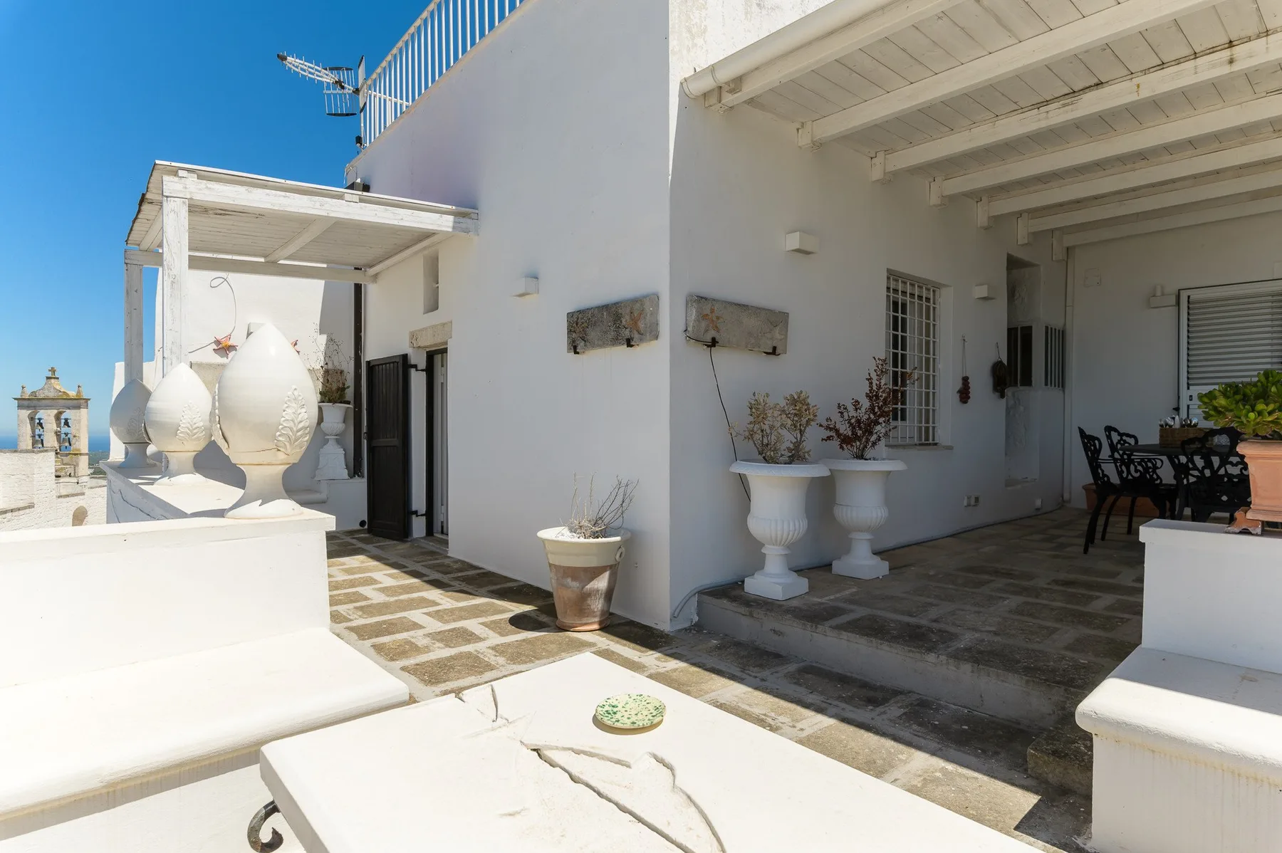 Un patio exterior luminoso con asientos blancos, jardineras y una zona de comedor a la sombra.