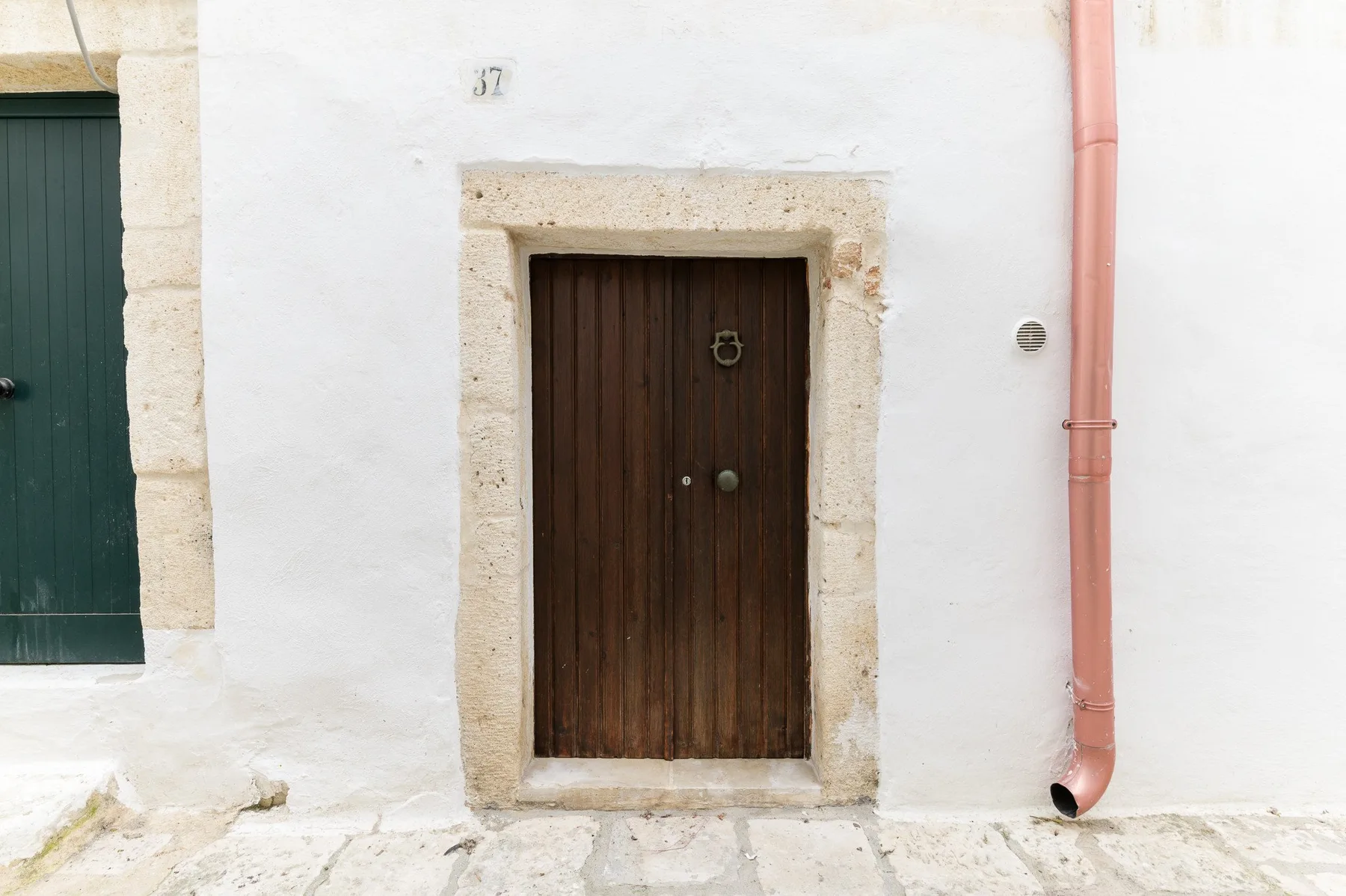 Una puerta de madera oscura en una pared exterior blanca junto a un tubo de desagüe rojo.