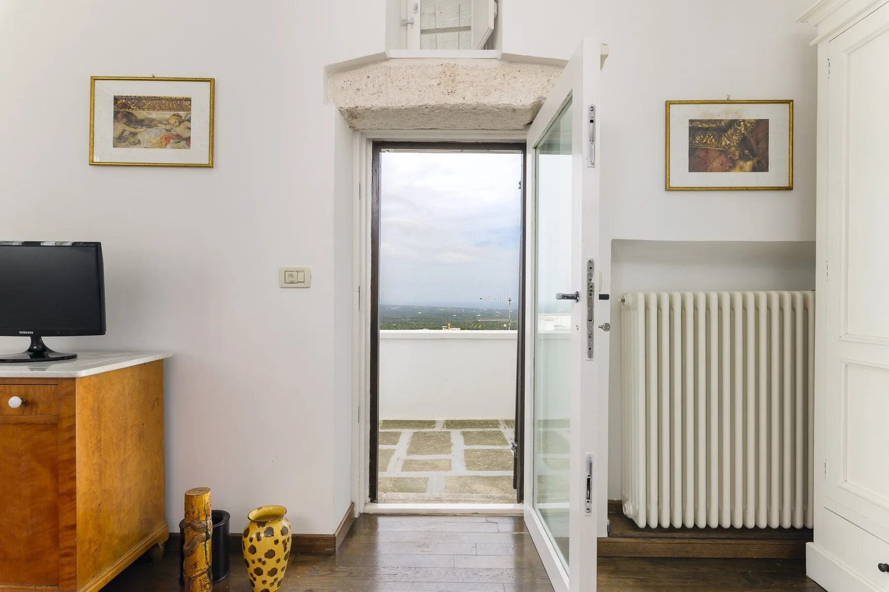 Una habitación luminosa se abre a un pequeño balcón pavimentado mediante una puerta de vidrio.