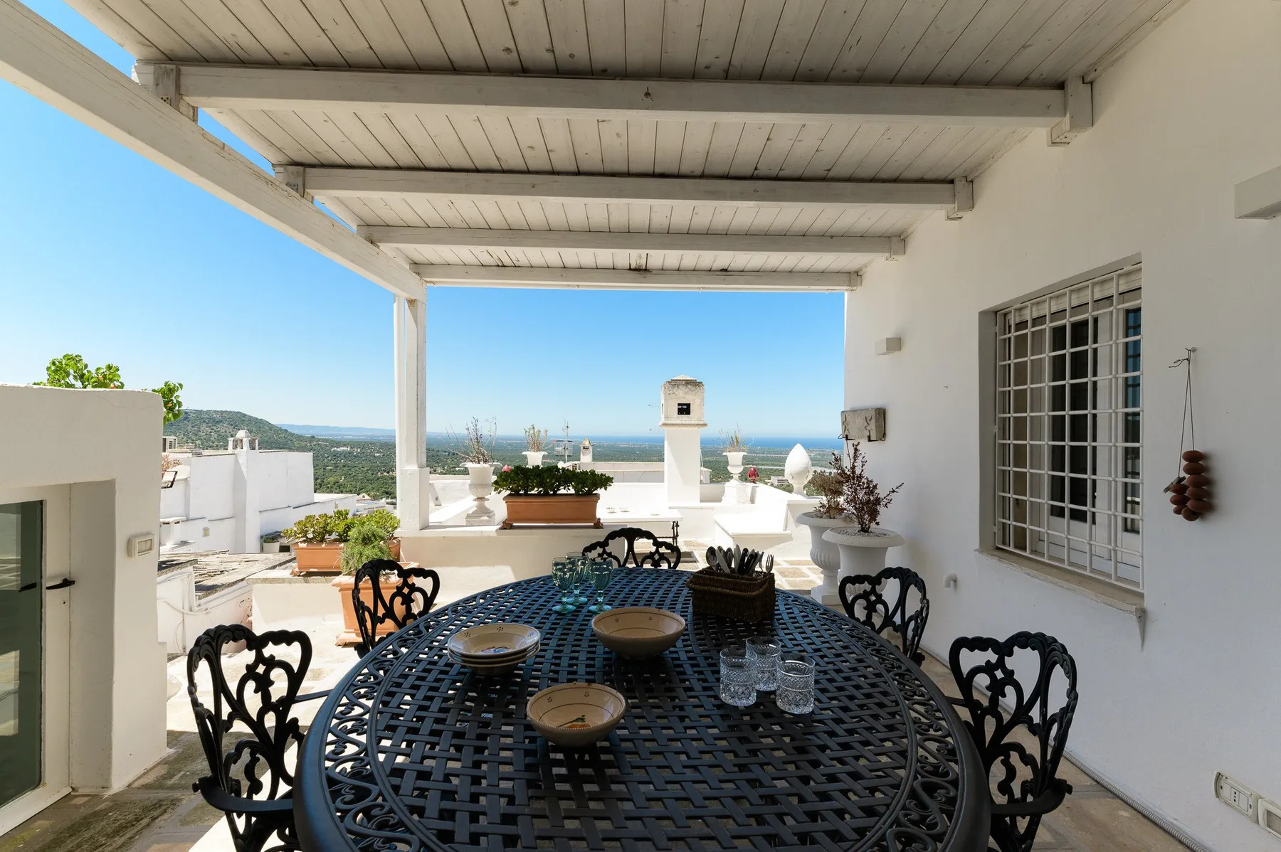 A covered rooftop terrace with a round outdoor table overlooking the sea.