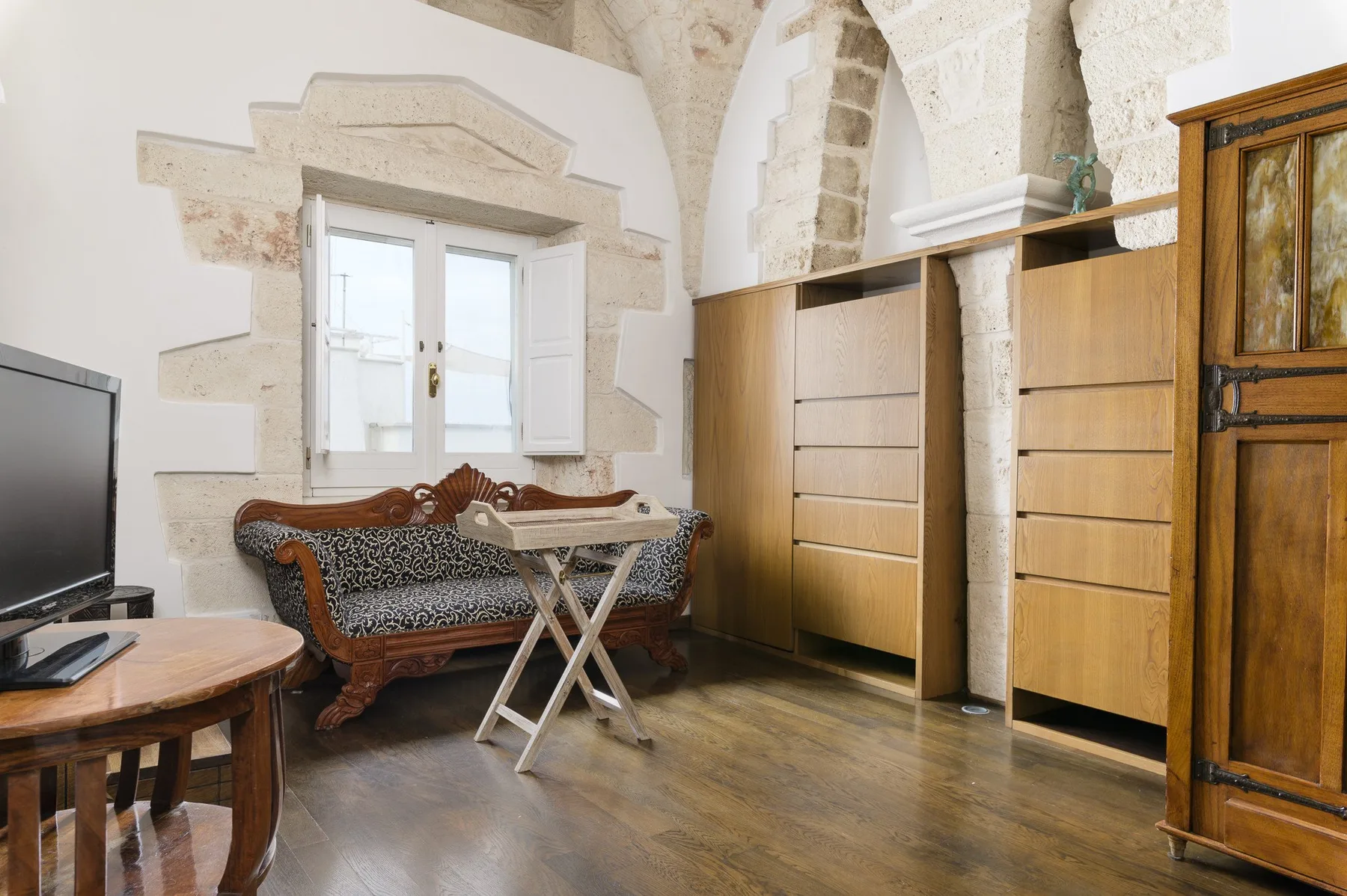 Una habitación amueblada con una ventana, armarios de madera y un sofá estampado.