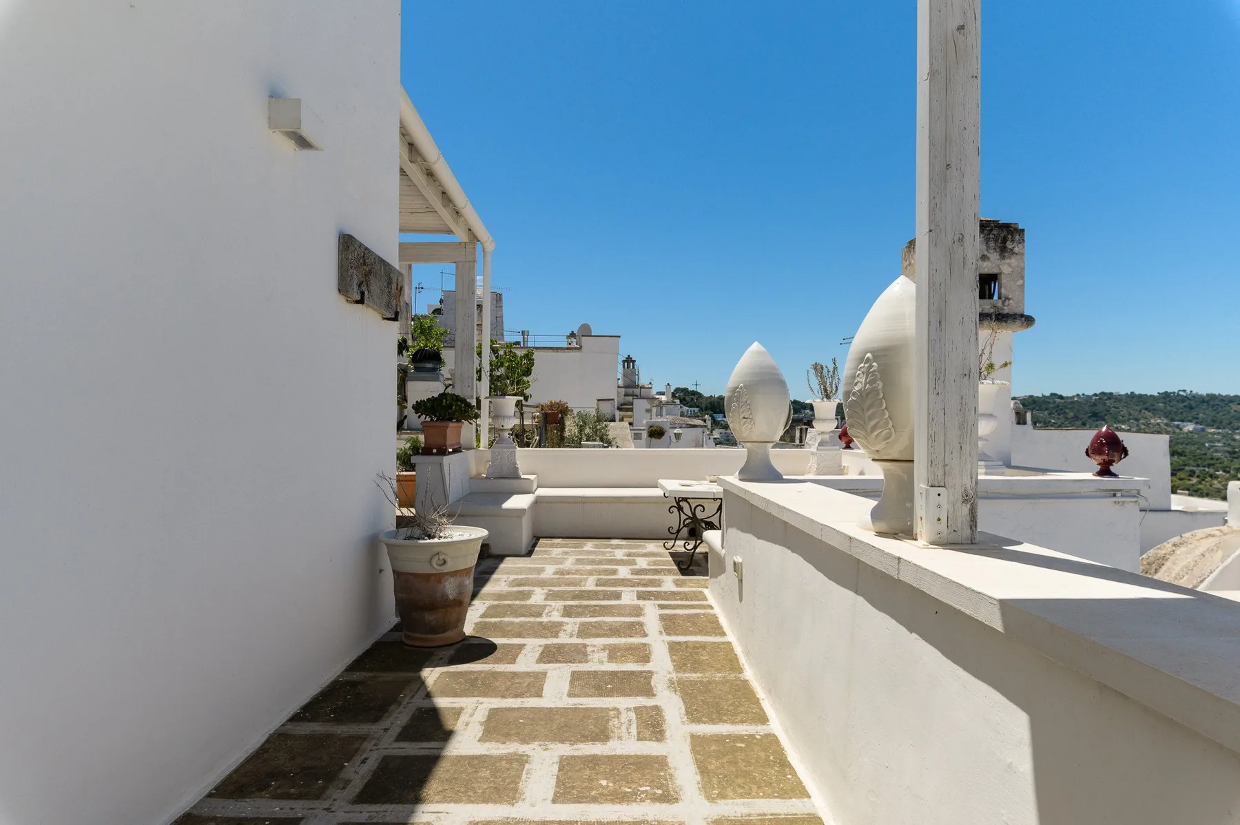 Una terraza soleada en la azotea con pavimento de piedra y adornos escultóricos blancos.
