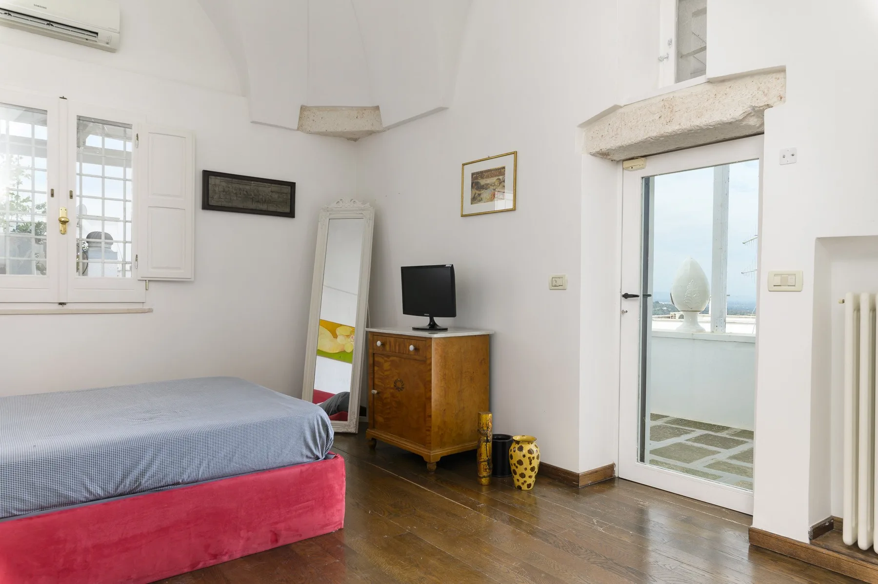 Un dormitorio con una cama, una cómoda de madera y una puerta que da a un balcón luminoso.