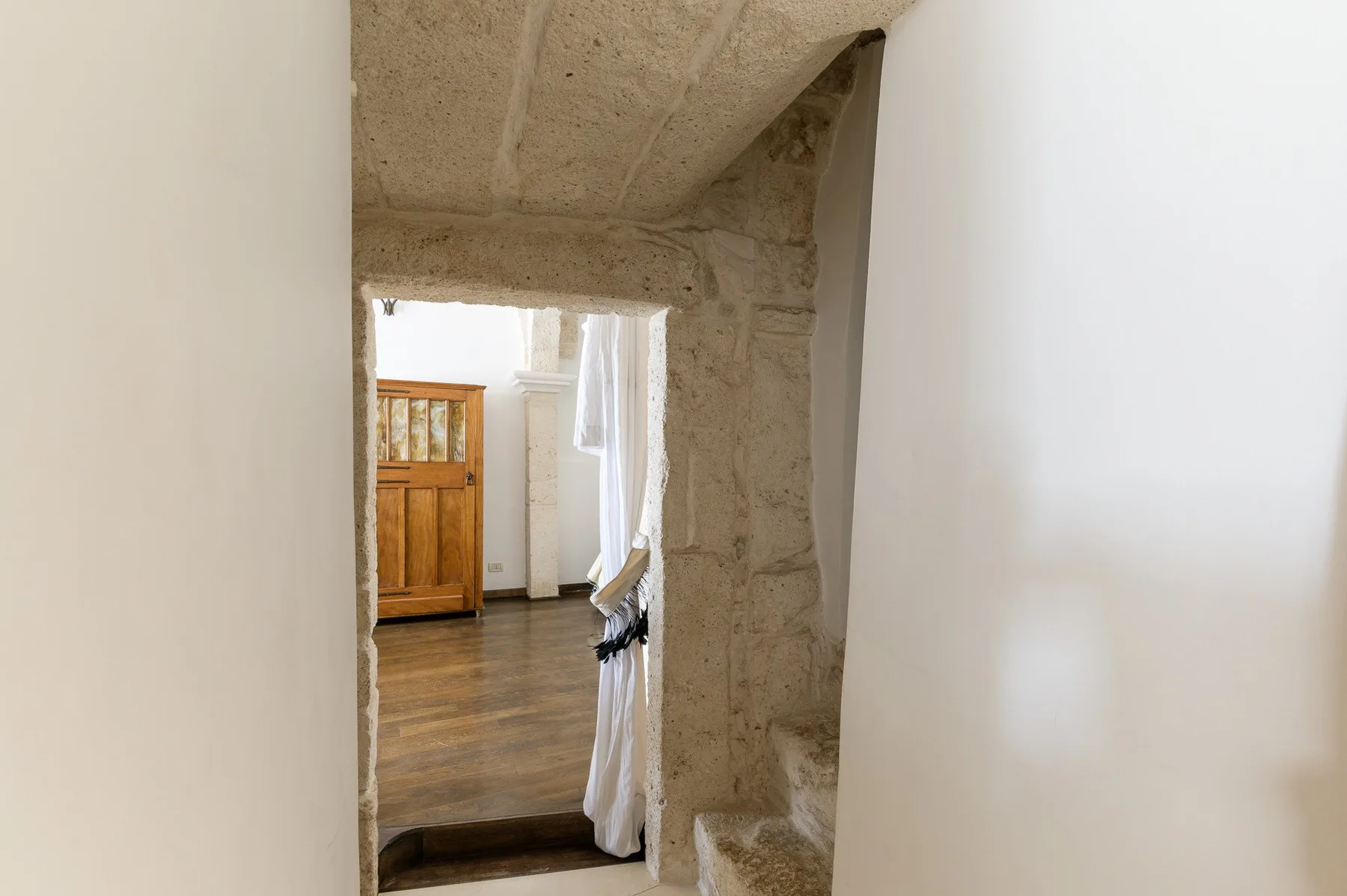 Una puerta de piedra da a una habitación luminosa con suelo de madera.