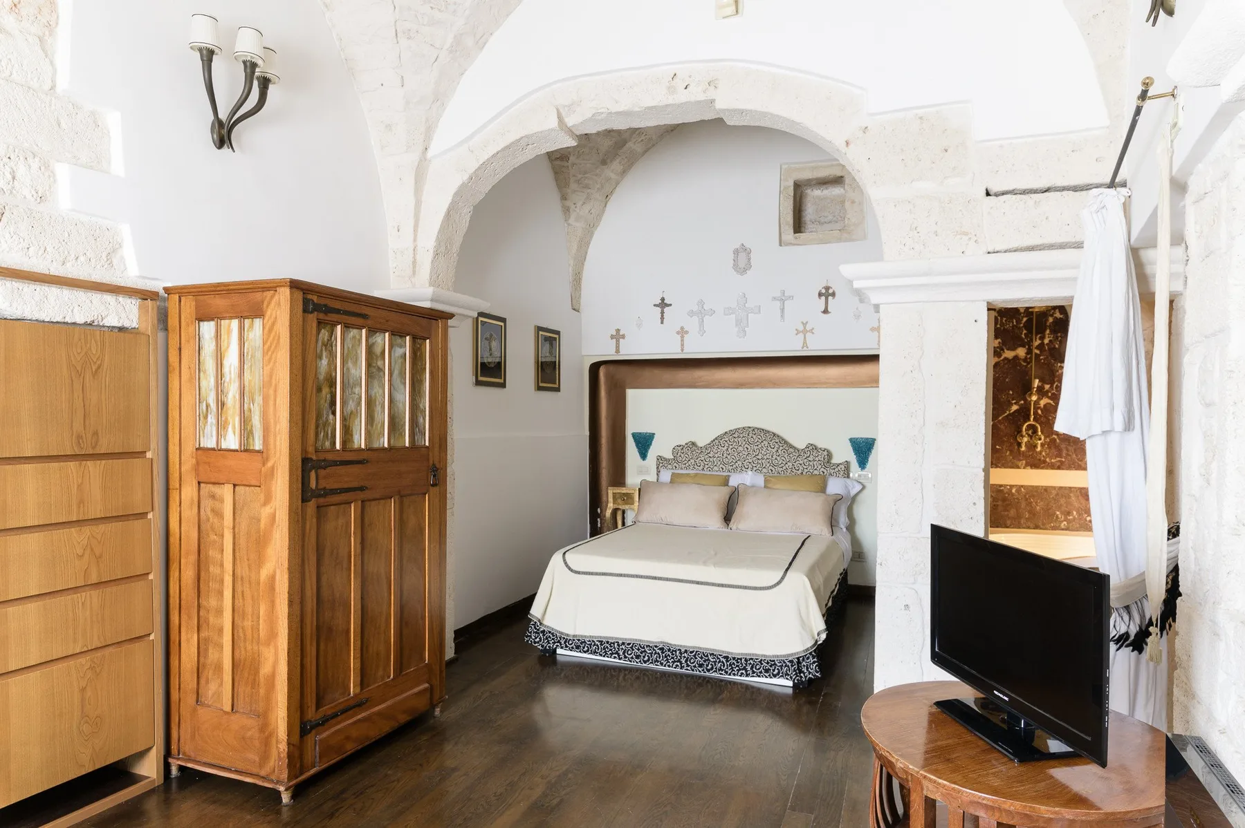 Un dormitorio con una cama bajo un arco de piedra y un televisor cerca.