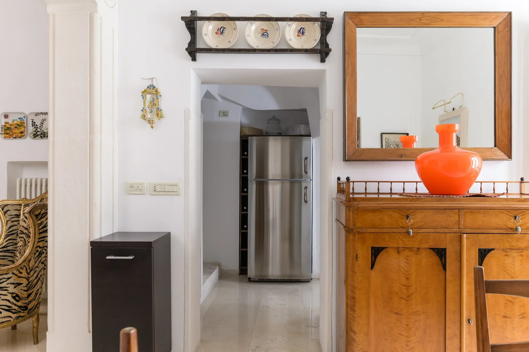 Un pasillo interior luminoso con un refrigerador en un vano y un mueble de madera.