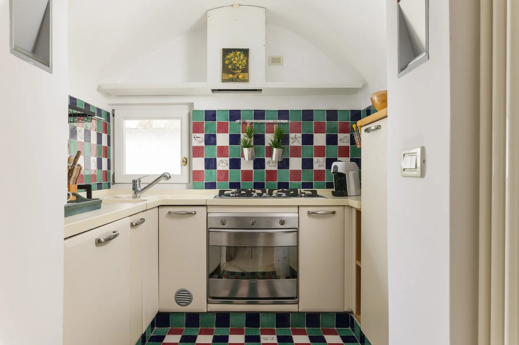 Una cocina compacta con azulejos cuadrados de colores y una ventana sobre el fregadero.