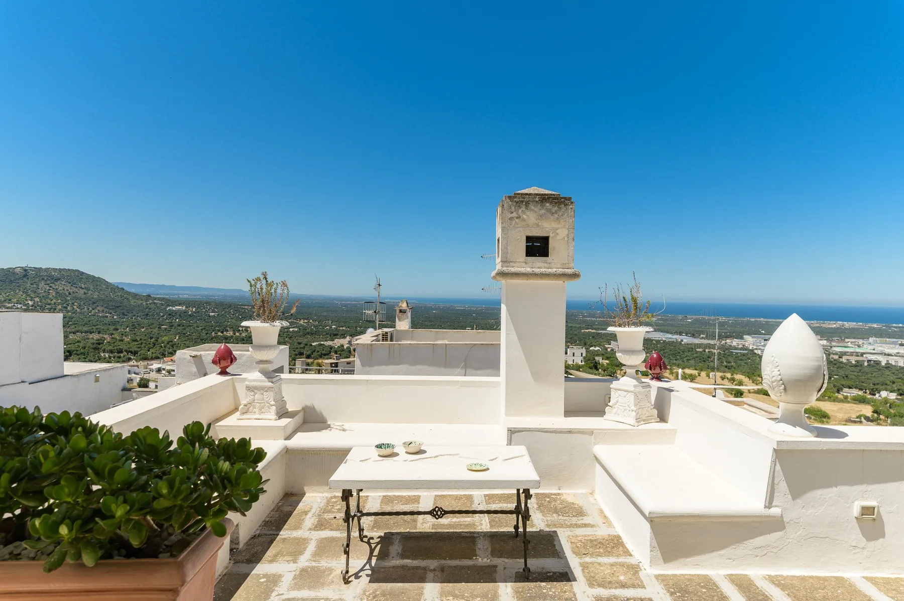 A sunny rooftop terrace with a table and wide views of the surrounding landscape.
