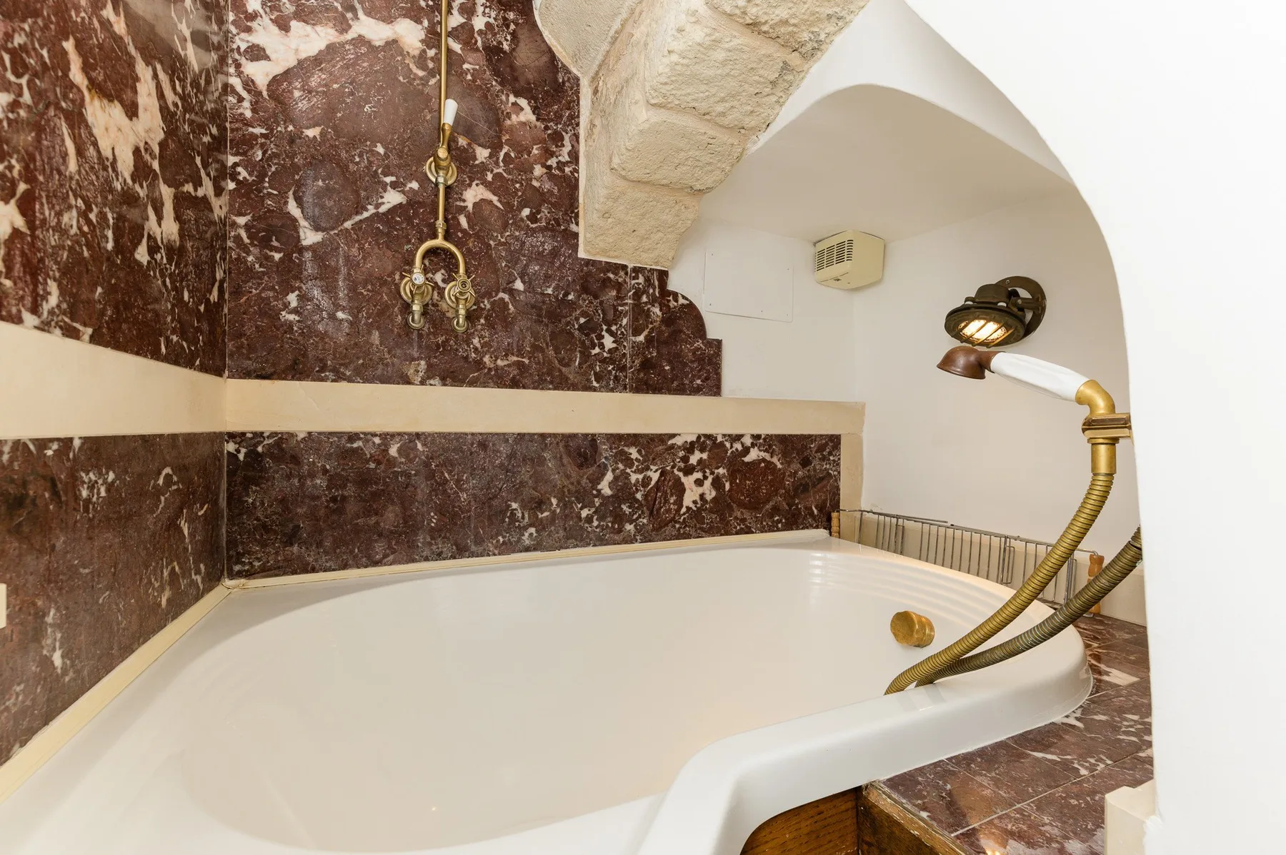 Una bañera empotrada está bajo un arco blanco curvo, junto a un grifo dorado.