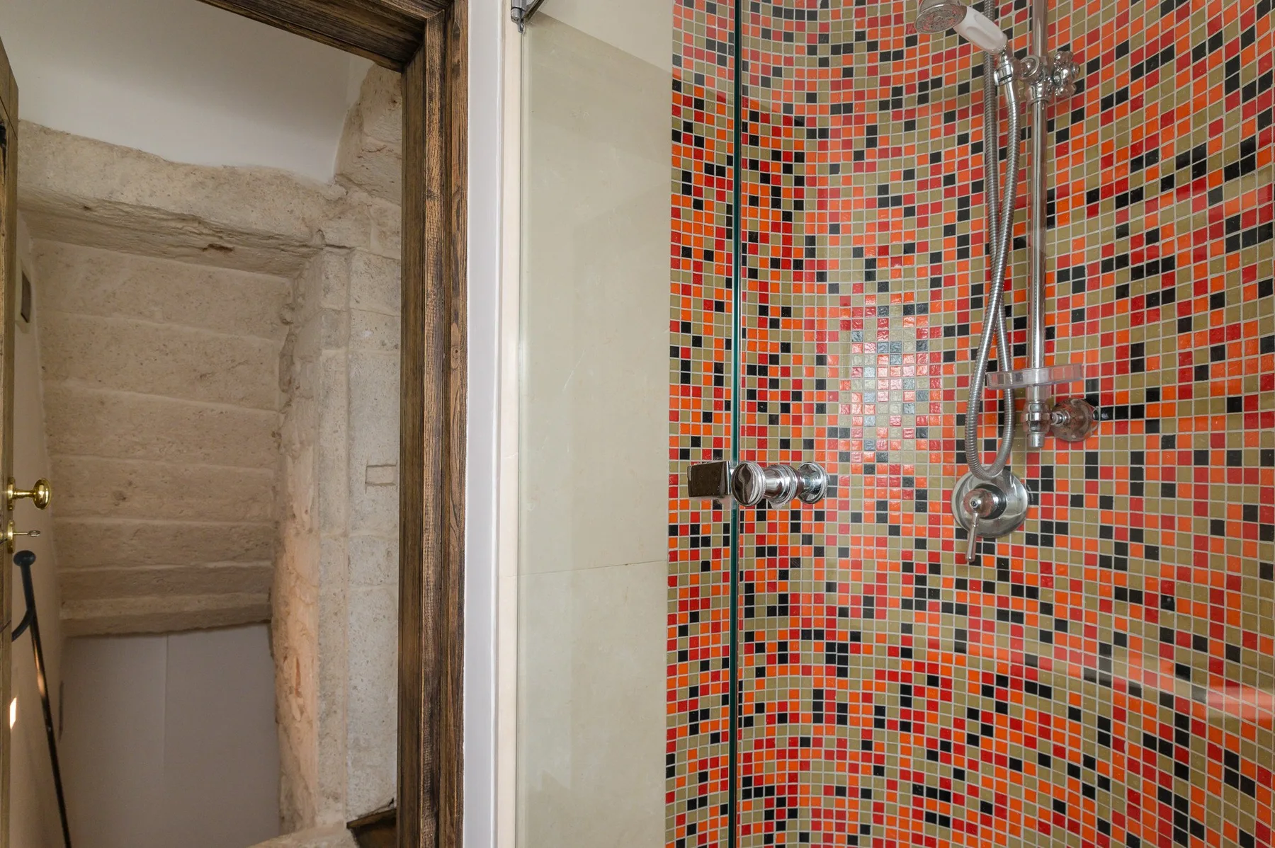 Una zona de ducha con paredes de mosaico colorido y accesorios metálicos.
