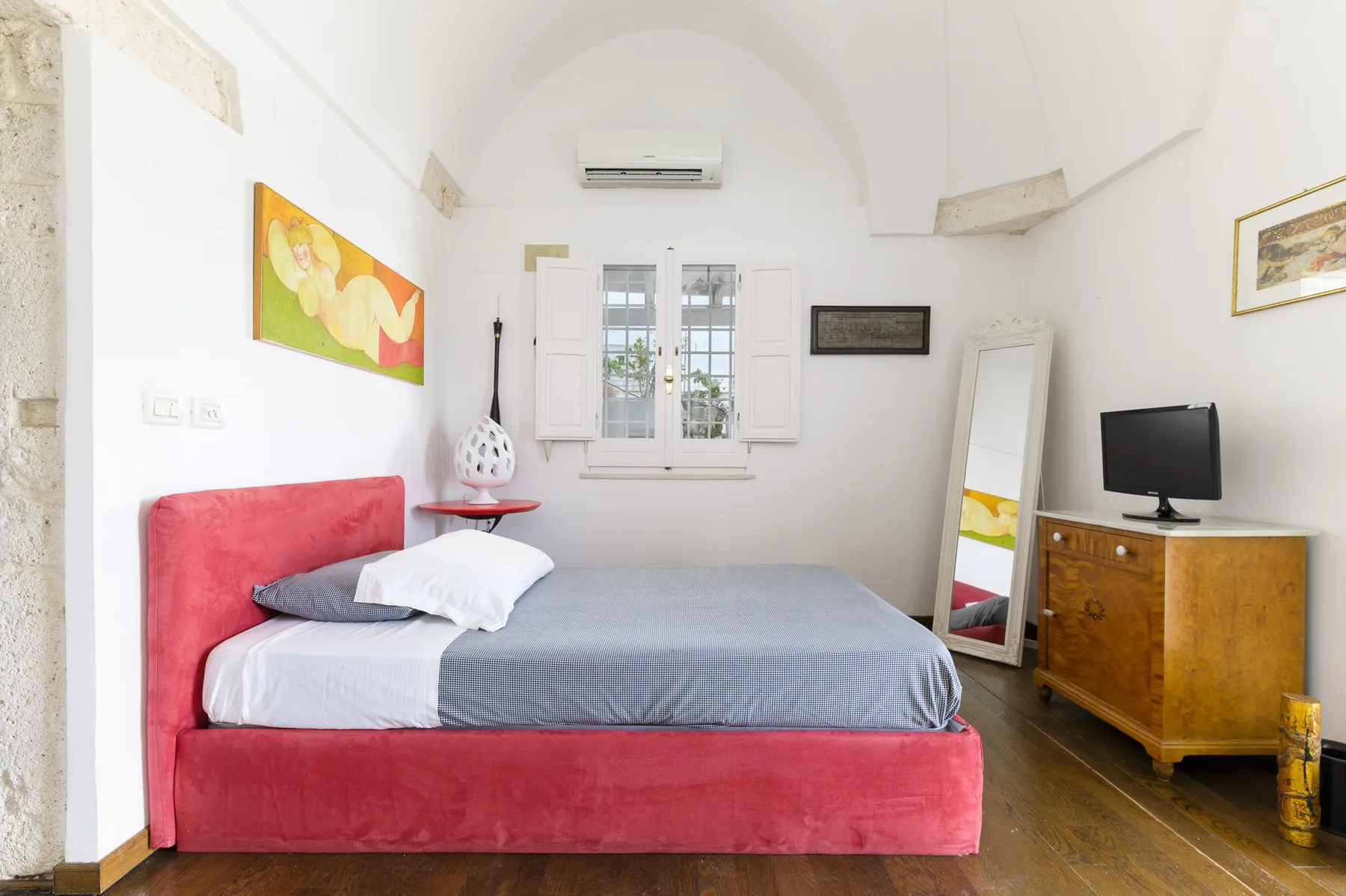 Un dormitorio con una cama tapizada roja, una ventana y una cómoda de madera.