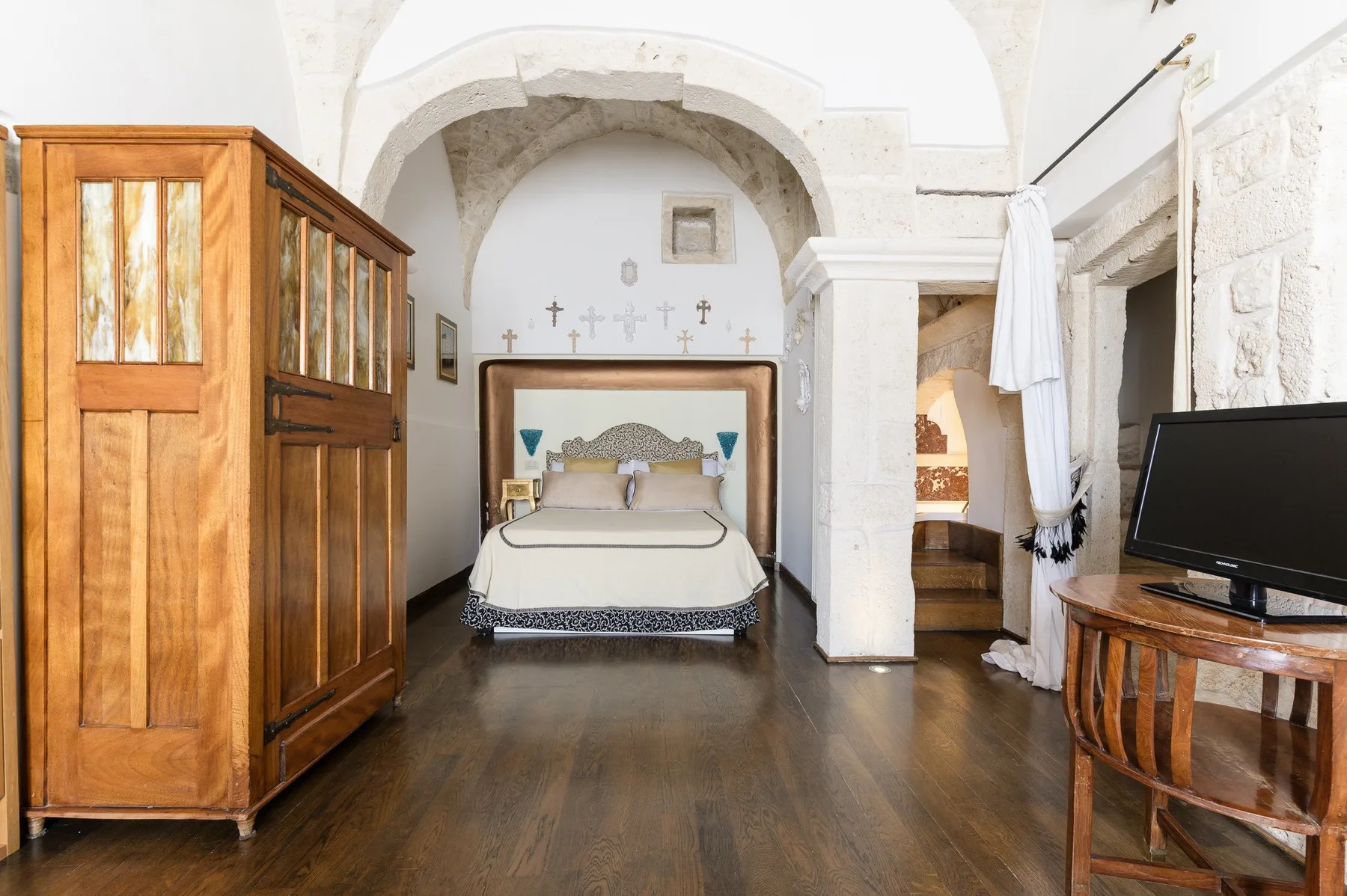 Un dormitorio con una cama bajo un arco de piedra y muebles de madera.