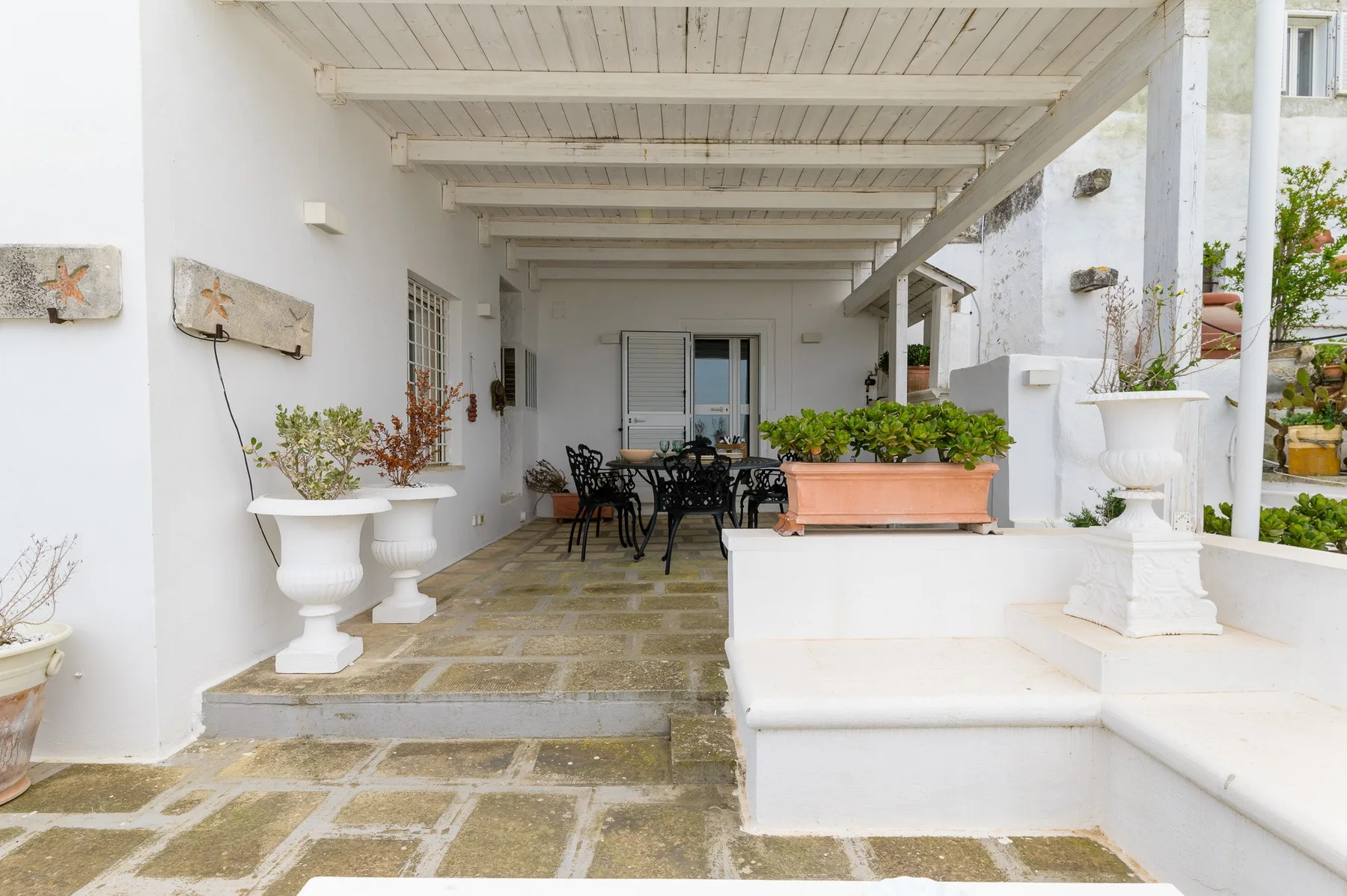 Comedor exterior cubierto con una mesa, asientos y plantas en macetas.