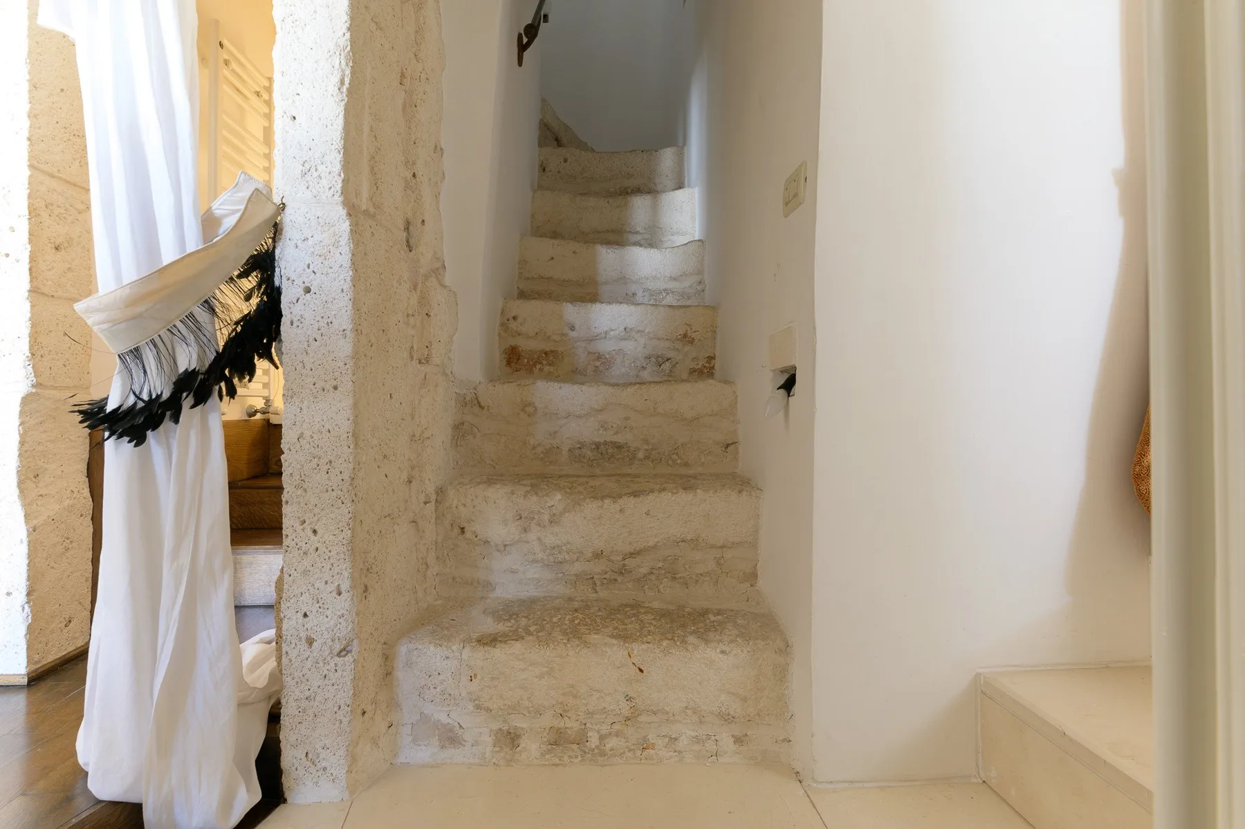 Una estrecha escalera de piedra sube entre paredes claras.