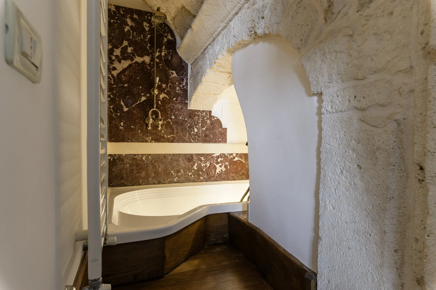Un baño con una bañera empotrada bajo un arco de piedra.
