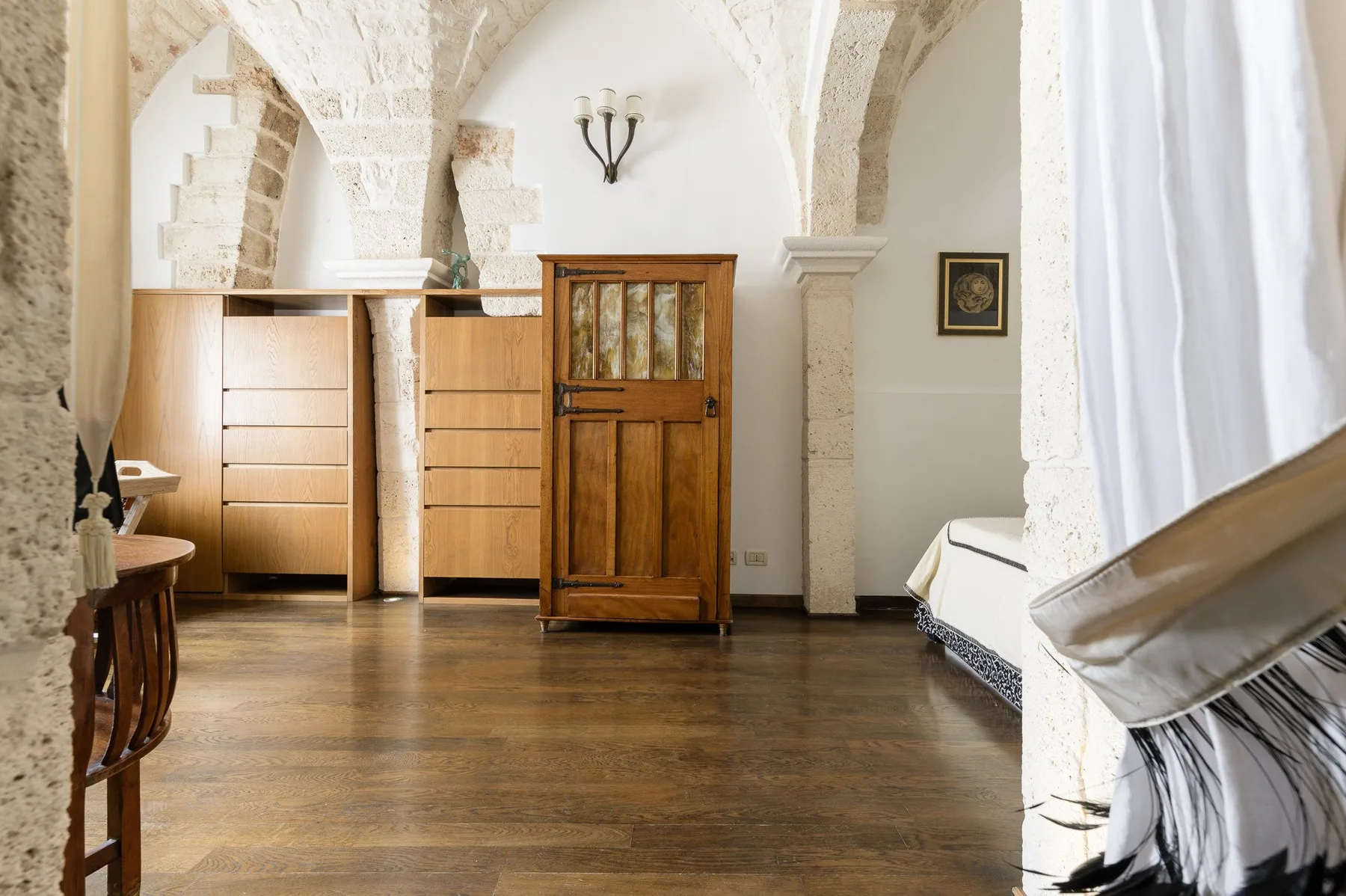 Una habitación con arcos de piedra, armarios de madera y una ventana con cortinas.