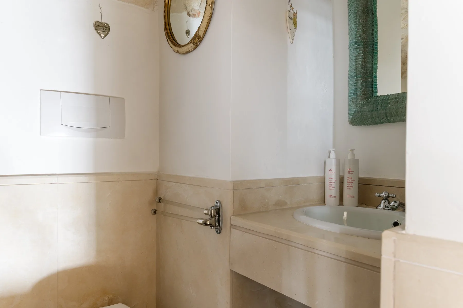 Un lavabo de baño con espejo, lavamanos y placa de descarga en la pared.