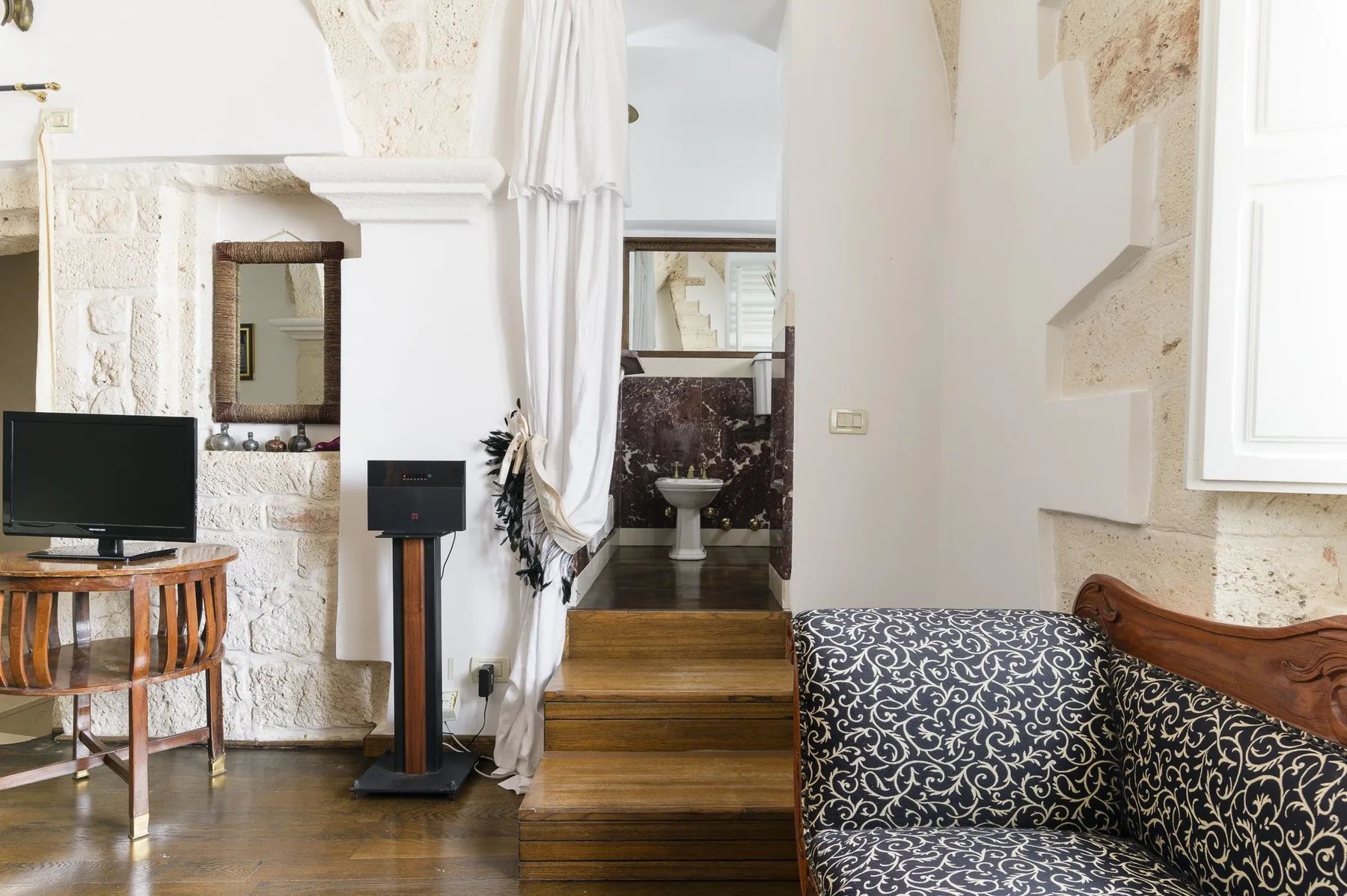 Una sala de estar con asientos estampados y escalones de madera hacia un baño.