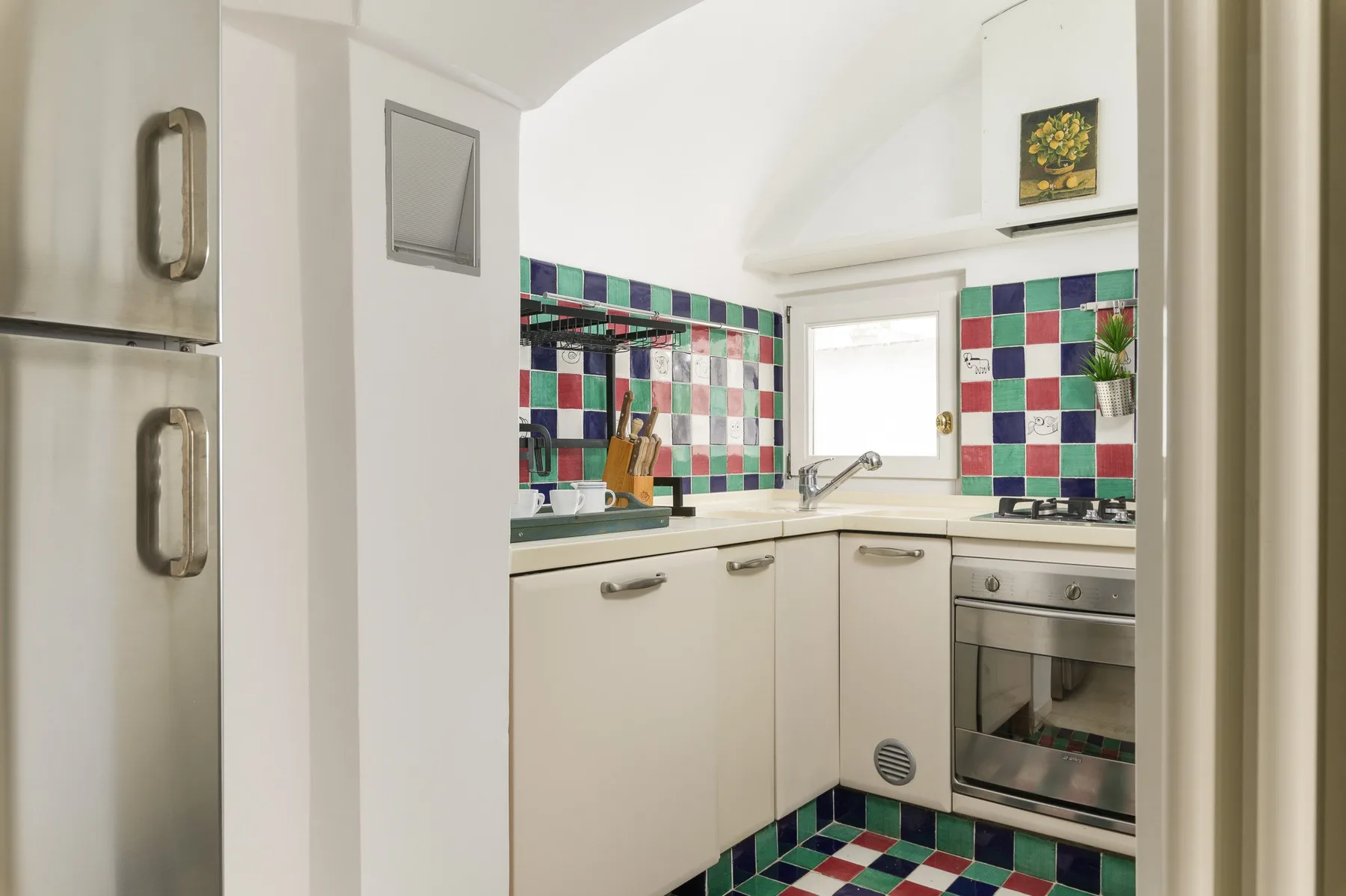Una cocina compacta con gabinetes blancos, un fregadero y paredes de azulejos coloridos.